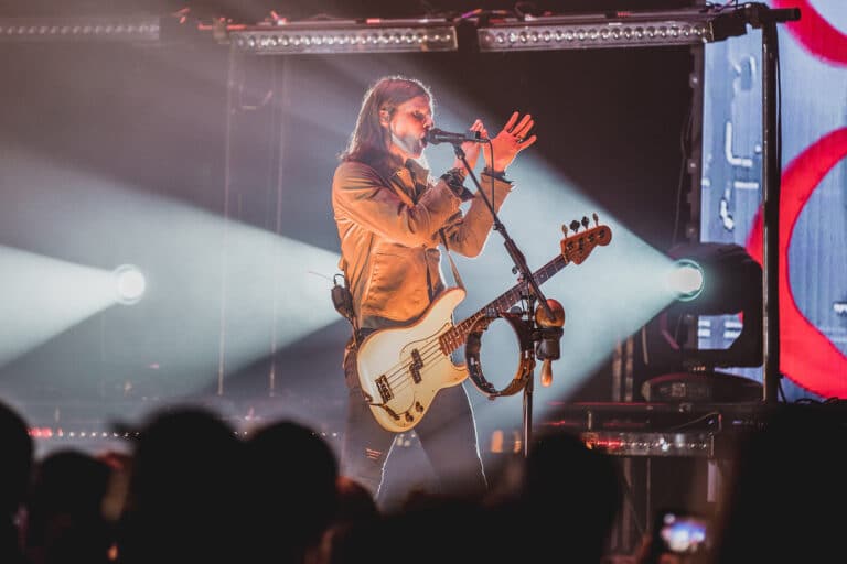 Musican with bass guitar engaging with crowd, clapping his hands on stage